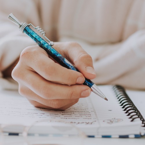 A vertical selective closeup of a female writing in a notebook with a blue pen